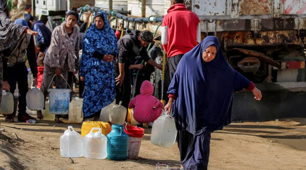يقوم الناس بملء خزانات المياه من صهريج متنقل في مخيم المغازي للاجئين الفلسطينيين وسط قطاع غزة (أ.ف.ب)