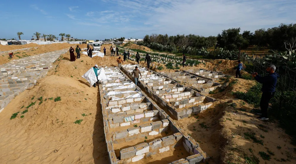 مواطنون يسيرون بجانب جثامين في مقبرة جماعية لفلسطينيين غير معلومي الهوية أفرجت عنهم إسرائيل في دير البلح (رويترز)