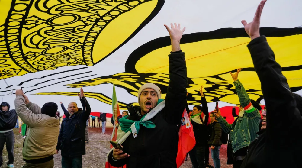 أنصار نجل الشاه رضا بهلوي يقفون تحت علم إيراني ضخم خلال مشاركتهم في مظاهرة في ميونيخ بألمانيا (أ.ب)