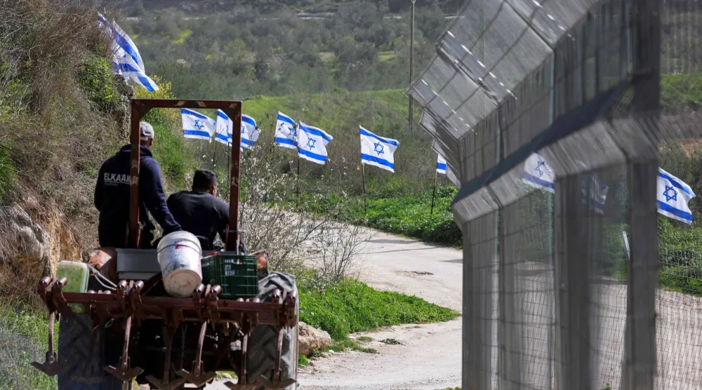 مزارعان فلسطينيان من قرية برقة في الضفة الغربية يستقلان جرارا بمحاذاة سياج نصبه مستوطنون أمس (أ.ف.ب)