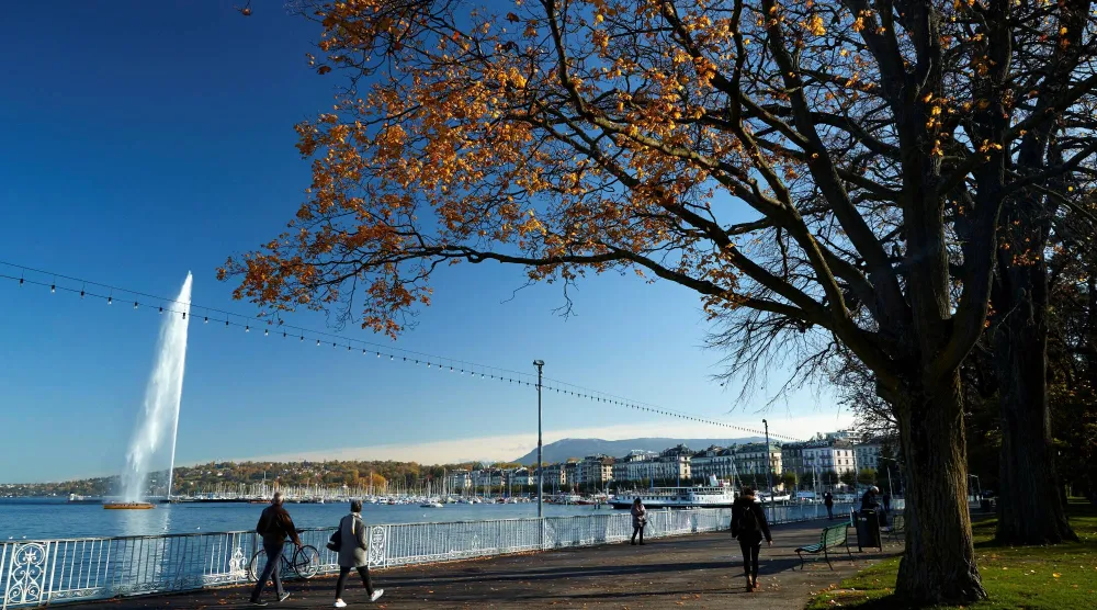 يمشي أشخاص بالقرب من بحيرة ليمان ونافورة المياه «جيت دو» في جنيف (رويترز)