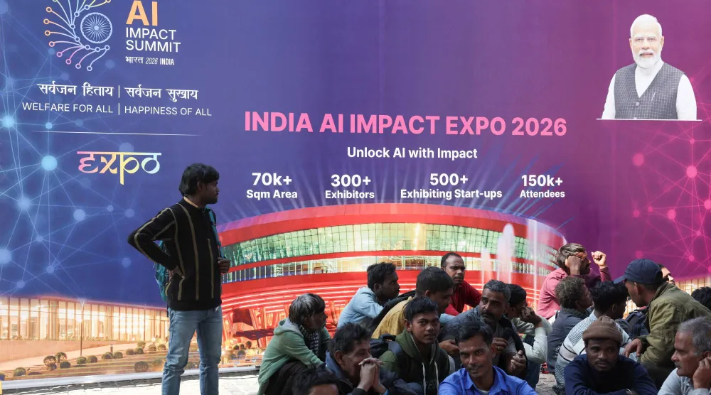 عمال يجلسون أمام لافتة «قمة تأثير الذكاء الاصطناعي» في الهند في بهارات ماندابام في نيودلهي (رويترز)