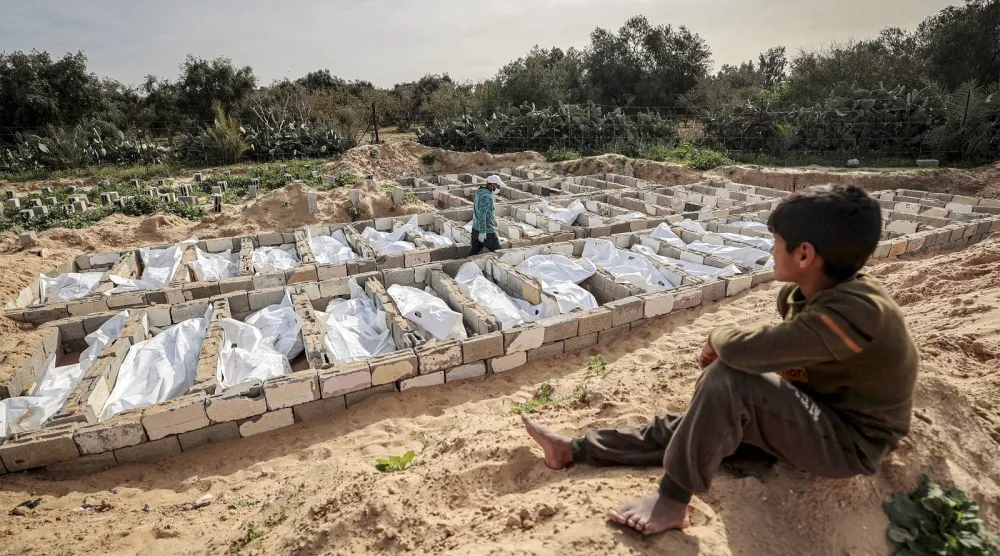 طفل فلسطيني صغير ينظر إلى دفن 53 جثة مجهولة الهوية في مقبرة في دير البلح بوسط قطاع غزة  (أ.ف.ب)
