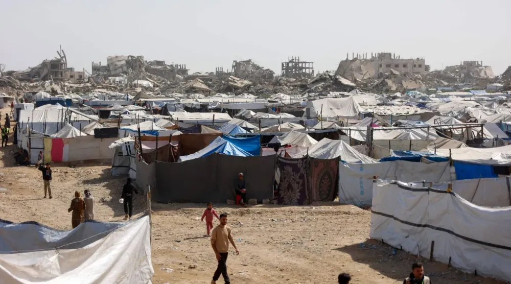 Dün Gazze şehrinde yıkılmış binaların yanında kurulan mülteci kampları arasında yürüyen Filistinliler (AFP)