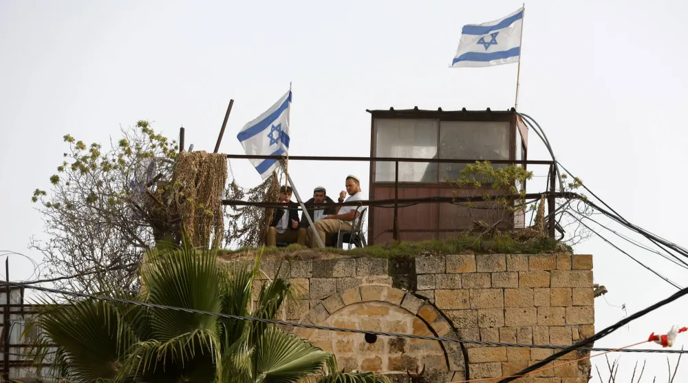  Israeli's sit on the roof next to a flag, as they monitor a weekly settlers' tour in Hebron, in the Israeli-occupied West Bank, February 14, 2026. (Reuters)