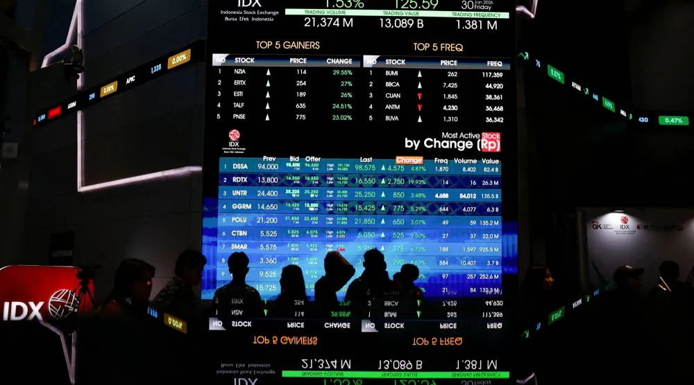 أشخاص يمرون أمام لوحة إلكترونية تعرض حركة الأسهم في بورصة إندونيسيا (رويترز)