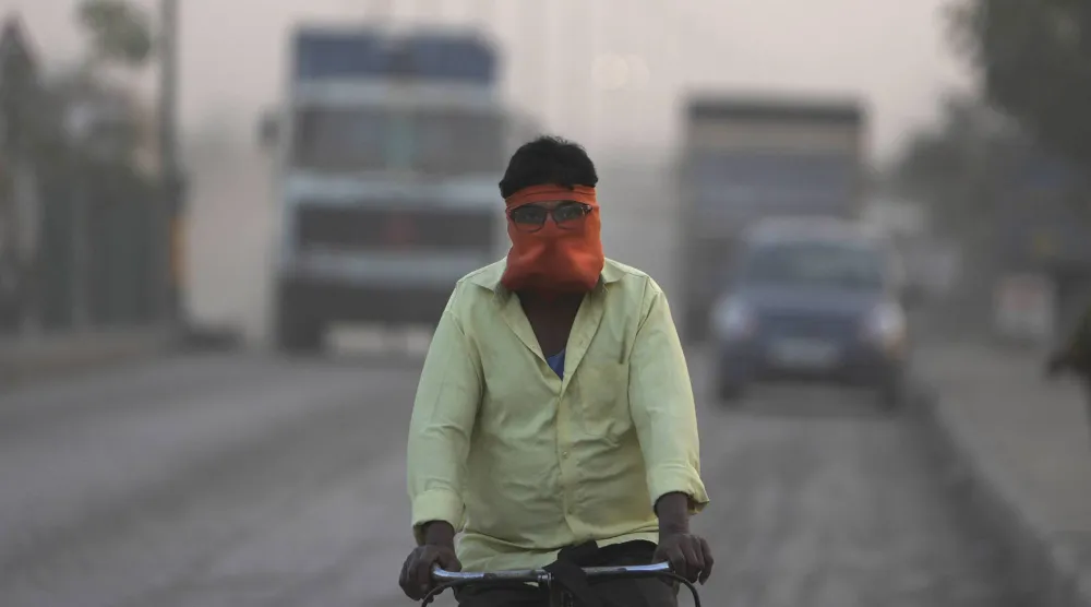 رجل يغطي وجهه في أثناء ركوبه دراجة وسط الغبار والتلوث في الهند (أ.ب)