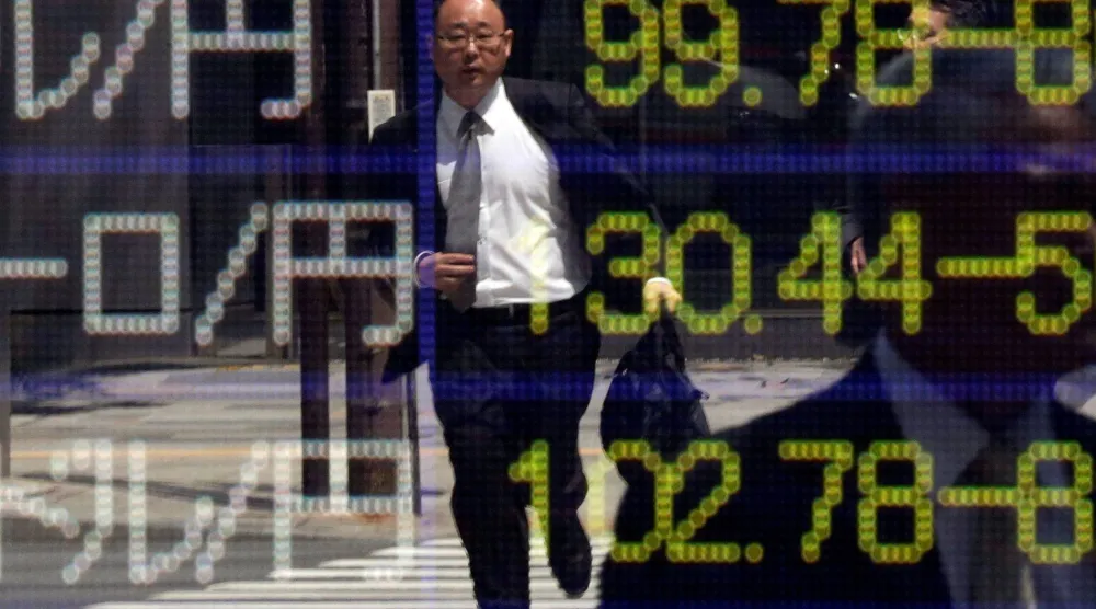 رجل يركض على ممر للمشاة ينعكس على لوحة إلكترونية تعرض أسعار الصرف خارج مكتب وساطة في طوكيو (رويترز)