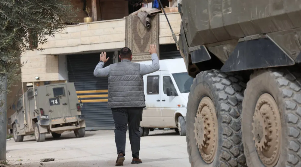 رجل فلسطيني يرفع يديه أثناء اعتقاله من قبل القوات الإسرائيلية خلال مداهمة عسكرية في جنين بالضفة الغربية (إ.ب.أ)