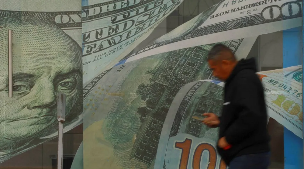 رجل يمر أمام محل صرافة مزين بلوحات من الفينيل عليها صور أوراق نقدية من فئة الدولار في سيوداد خواريز بالمكسيك (رويترز)