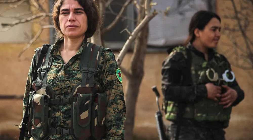 روكسان محمد 37 عاماً (يسار) المتحدثة باسم وحدات حماية المرأة تنتظر برفقة مقاتلات من قوات الأمن الداخلي حاملةً رشاشها بالقرب من مطار القامشلي في 8 فبراير (أ.ف.ب)