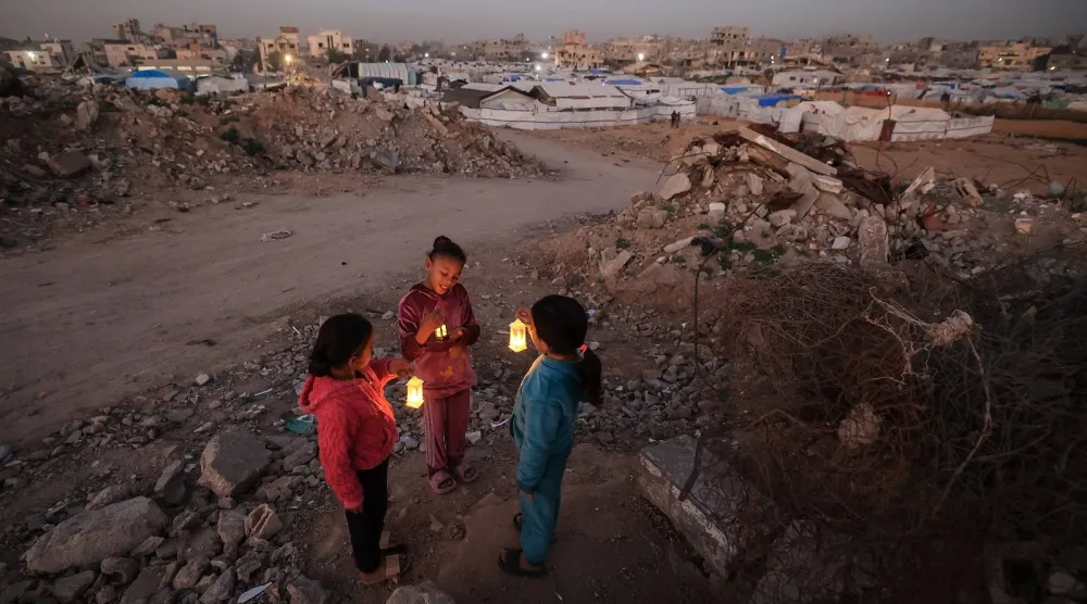 شبان فلسطينيون نازحون يلعبون على أنقاض المباني المدمرة حاملين فوانيس رمضان في مخيم البريج للاجئين وسط قطاع غزة (أ.ف.ب)