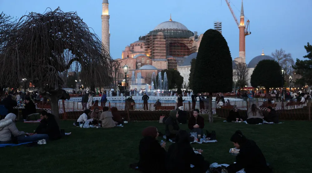 صائمون وقت الإفطار في ساحة مسجد السلطان أحمد بمدينة إسطنبول التركية ويبدو في الخلفية مسجد أيا صوفيا (رويترز)