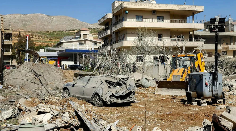 جرّافة تزيل الأنقاض بالقرب من مبانٍ متضررة بشدة بقرية بدنايل بمنطقة سهل البقاع الشرقية في لبنان (أ.ف.ب)