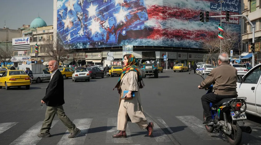 Pedestrians walk past a billboard depicting a US aircraft carrier with damaged fighter jets on its deck and a sign in Farsi and English reading, "If you sow the wind, you'll reap the whirlwind," in Tehran, Iran, Sunday, Feb. 22, 2026. (AP Photo/Vahid Salemi)