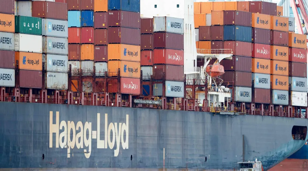 سفينة تعبر بجانب سفينة حاويات محملة بحاويات شحن في ميناء لوس أنجليس (أ.ف.ب)