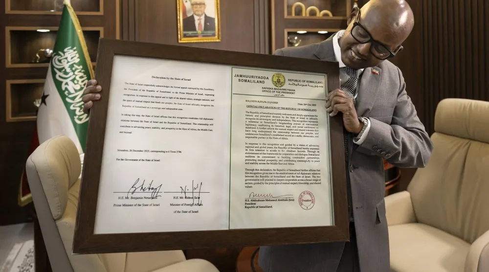وزير رئاسة جمهورية أرض الصومال خضر حسين عبدي يقف أمام شهادة مؤطرة تحتوي على إعلان موقع من إسرائيل بالاعتراف بأرض الصومال كدولة (أ.ف.ب)