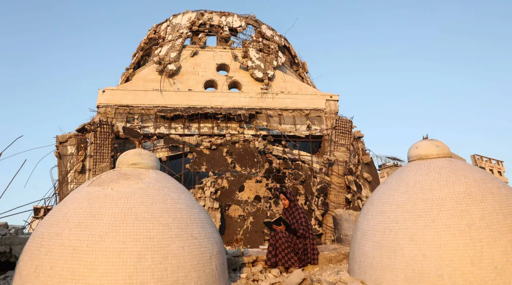 A female member of the al-Ghafir family, sits of the debris of the al-Hasayna Mosque as she recites from a copy of the Quran, during the holy month of Ramadan in western Gaza City on February 21, 2026. (Photo by Omar AL-QATTAA / AFP)