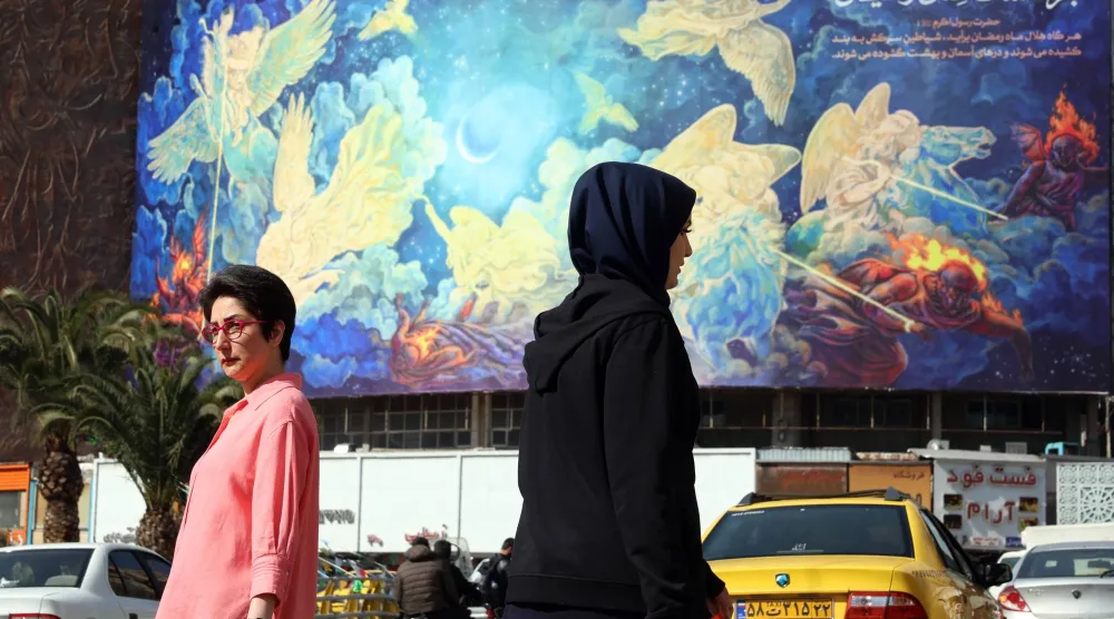 إيرانيات يسرن في طهران وخلفهن لوحة مكتوب عليها «الإنسان سوف يغلب الشيطان» (إ.ب.أ)