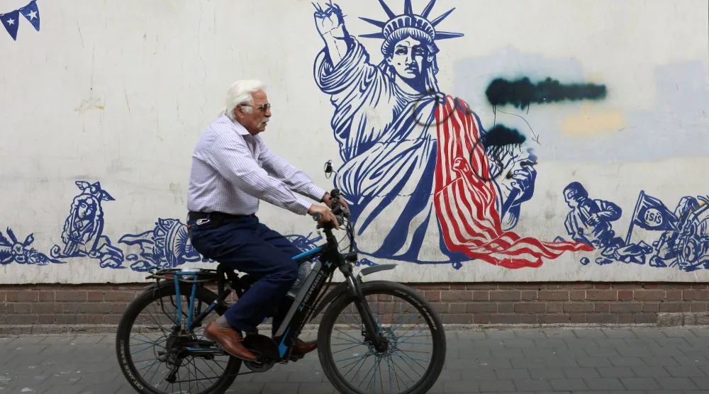 إيراني مسن يركب دراجة هوائية بجوار جدارية مناهضة للولايات المتحدة في طهران (إ.ب.أ)