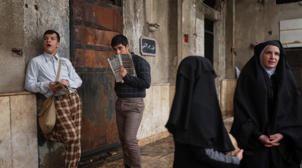 Extras stand by as a television crew films an episode of the TV series “Al-Souriyoun al-Aada” (“The Syrian Enemies”), based on a novel of the same name that was banned under Bashar Assad, along a transformed street in central Aleppo, Syria, Friday, Feb. 13, 2026. (AP Photo/Ghaith Alsayed)

