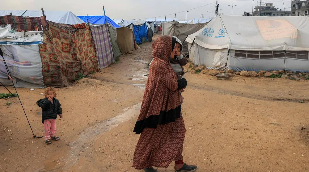 نازحة فلسطينية تسير حاملة طفلها على أرض بللتها مياه الأمطار بمخيم البريج للاجئين بوسط قطاع غزة يوم الثلاثاء (أ.ف.ب)