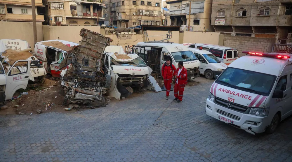 يسير مسعفون فلسطينيون أمام سيارات إسعاف مدمرة في مقر جمعية الهلال الأحمر الفلسطيني في خان يونس جنوب قطاع غزة (أ.ف.ب)