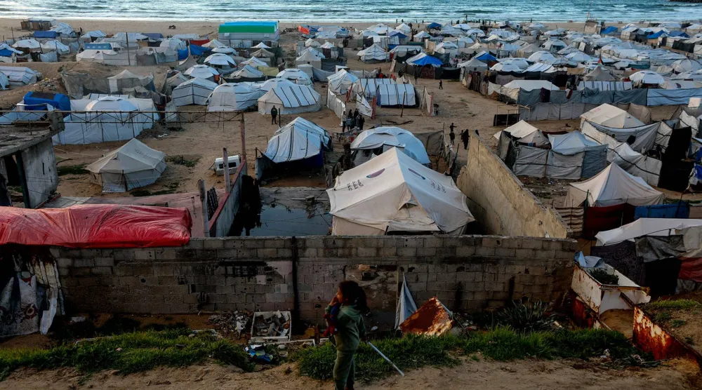 طفلة فلسطينية نازحة وخلفها خيام مؤقتة قرب شاطئ مدينة غزة (إ.ب.أ)