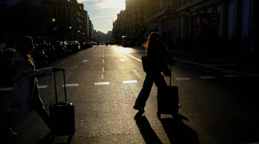 سياح يجرون أمتعتهم عند وصولهم إلى ساحة كاتالونيا في برشلونة (رويترز)