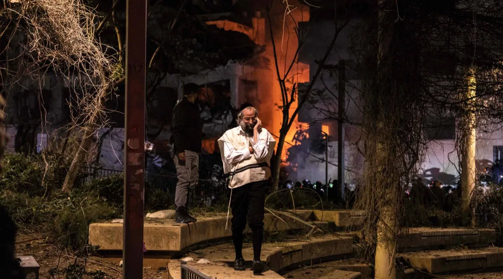 إسرائيلي يتحدث عبر هاتفه النقال بالقرب من موقع سقوط صاروخ إيراني وسط مدينة تل أبيب (أ.ف.ب)