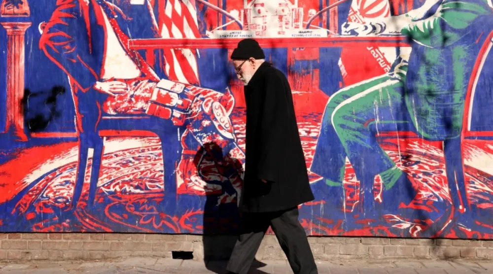 İran rejimi tarafından “casus yuvası” olarak adlandırılan Tahran'daki eski ABD büyükelçiliğinin dış duvarlarına çizilmiş bir duvar resminin önünden geçen bir adam, 1 Şubat 2026(AFP)