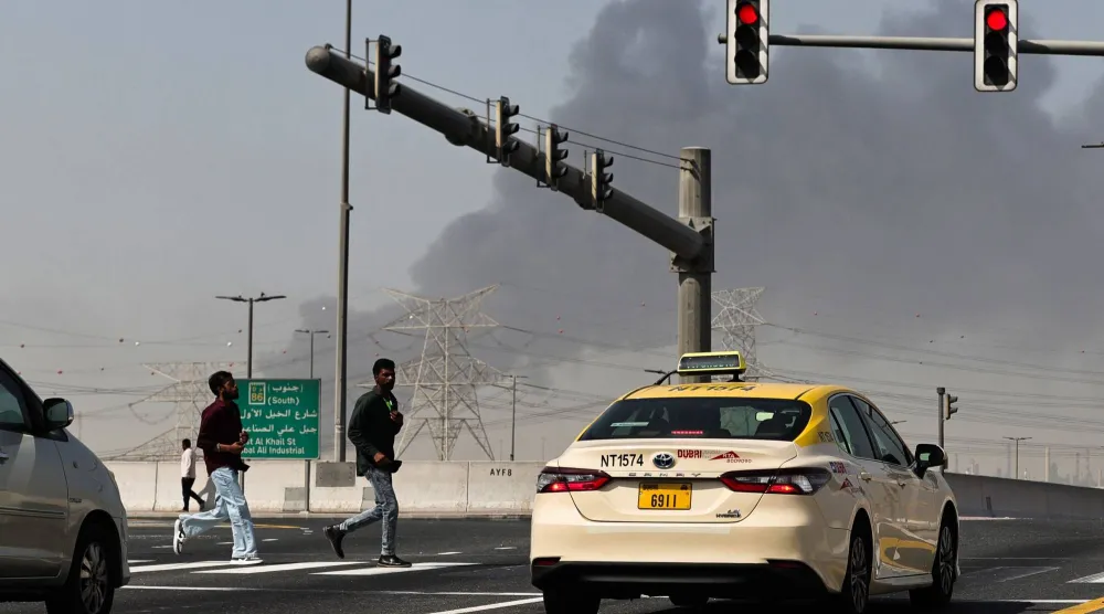 يعبر الناس شارعاً بينما يتصاعد الدخان من موقع سقوط شظايا بسبب التصدي لغارة إيرانية على دبي (أ.ف.ب)