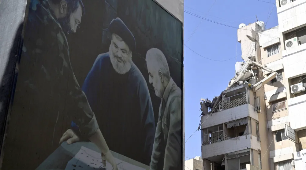 صورة تجمع قاسم سليماني ونصر الله وعماد مغنية مرفوعة على مبنى في ضاحية بيروت الجنوبية قرب موقع الاستهداف الإسرائيلي في حارة حريك (إ.ب.أ)