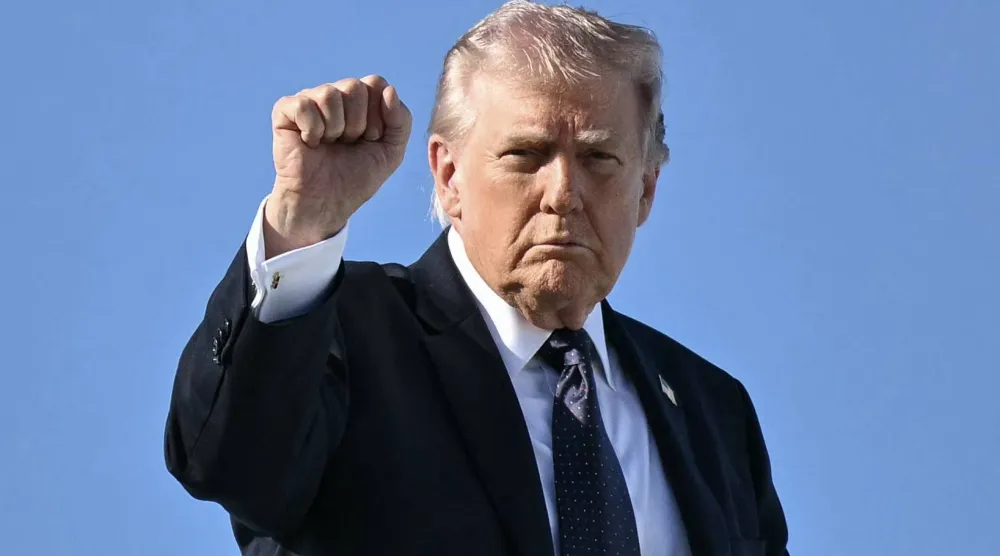 الرئيس الأميركي دونالد ترمب يشير بقبضته على سلم الطائرة الرئاسية المتجهة إلى واشنطن (أ.ف.ب)