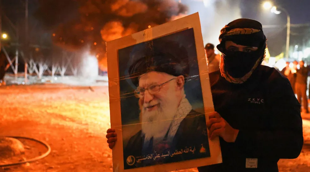 متظاهر في بغداد يحمل صورة المرشد الأعلى الإيراني علي خامنئي بعد إعلان مقتله (رويترز)