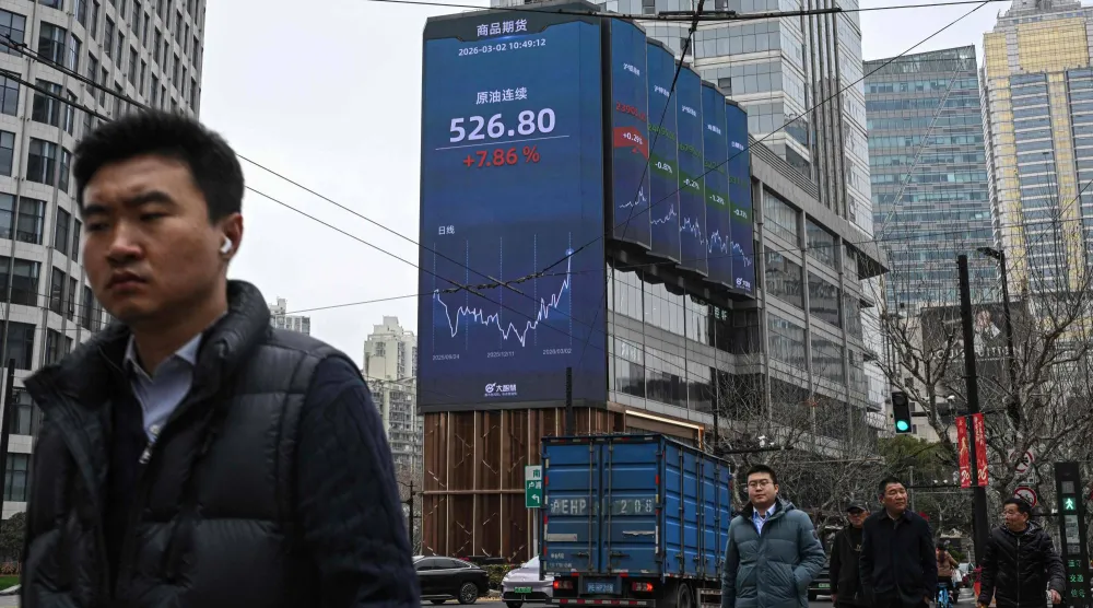 يسير المارة بجوار شاشة تعرض أسعار العقود الآجلة للنفط الخام في منطقة جينغان بشنغهاي (أ.ف.ب)