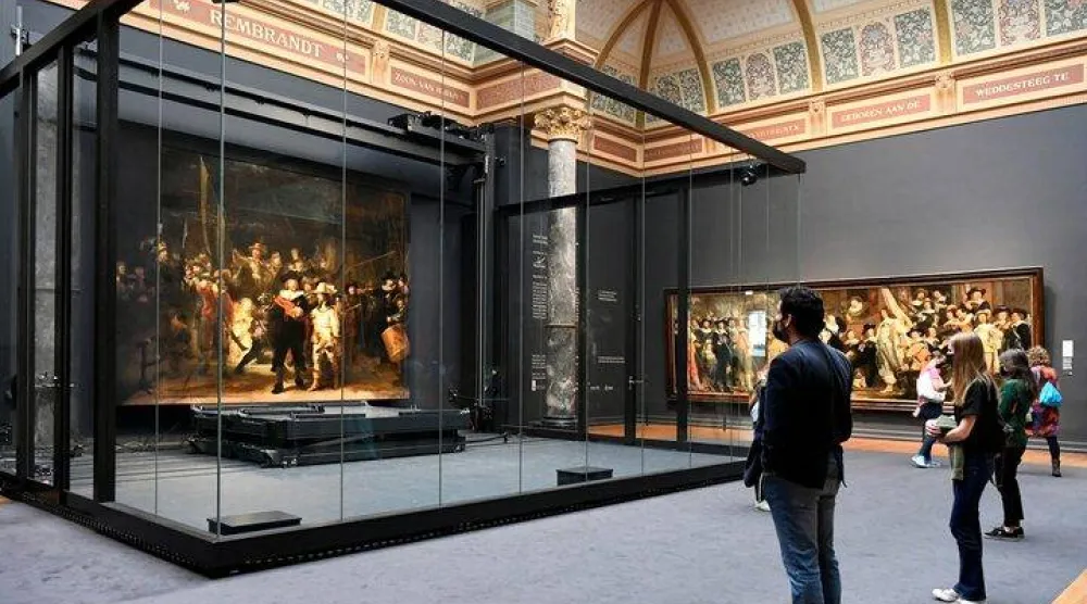Poeple look at Rembrandt's famed Night Watch, which is back on display in what researchers say in its original size, with missing parts temporarily restored in an exhibition aided by artificial intelligence, at Rijksmuseum in Amsterdam, Netherlands June 23, 2021. REUTERS/Piroschka van de Wouw/File Photo
