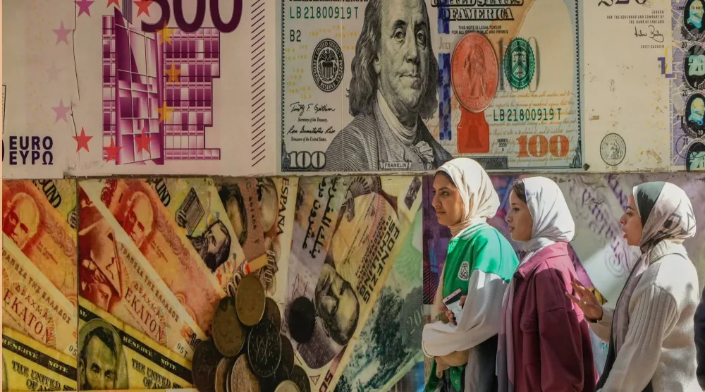 مصريات يسِرن أمام ملصق يصور الدولار الأميركي وعملات أخرى خارج مكتب صرافة في القاهرة (أ.ب)