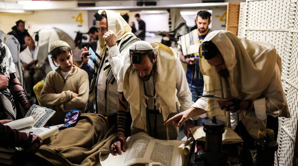 إسرائيليون يقرؤون يوم الثلاثاء من سفر ديني في موقف سيارات تحت الأرض يُستخدم كملجأ (رويترز)