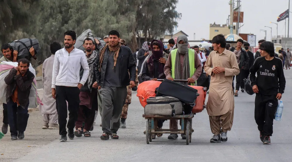 مواطنون أفغان بالقرب من جسر الحرير بعد عودتهم من إيران عند معبر حدودي (أ.ف.ب)