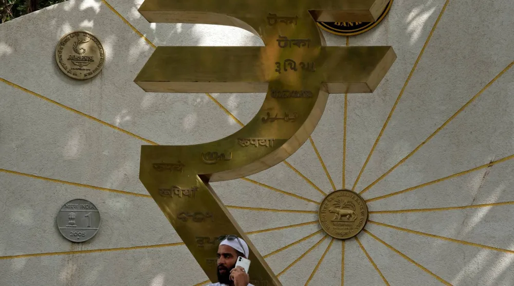 رجل يتحدث عبر هاتفه المحمول بجوار مجسم لشعار الروبية وعملات العملة الهندية خارج مقر بنك الاحتياطي الهندي في مومباي (رويترز)