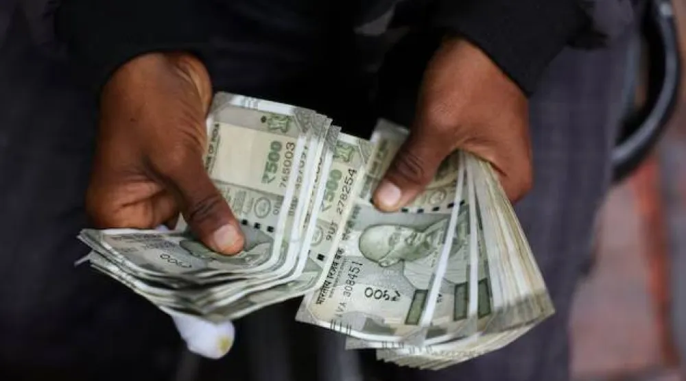 رجل يَعدّ أوراقاً نقدية هندية عند كشك صرافة على جانب الطريق بالأحياء القديمة من دلهي (رويترز)