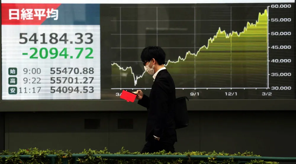 رجل يمر أمام شاشة تعرض حركة الأسهم في وسط العاصمة اليابانية طوكيو (رويترز)