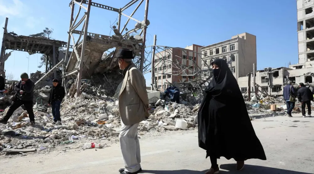 Tahran'ın merkezinde hava saldırıları sonucu hasar görmüş bir binanın önünden bir erkek ve bir kadın geçiyor (AFP)