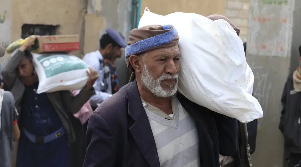 رجل يحمل جوال مساعدات غذائية في منطقة بغرب اليمن (إ.ب.أ)