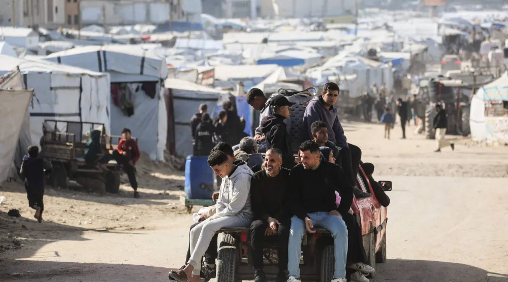 فلسطينيون يستقلون شاحنة صغيرة يمرون بمئات الخيام المنصوبة لإيواء الفلسطينيين النازحين في خان يونس (أ.ف.ب)