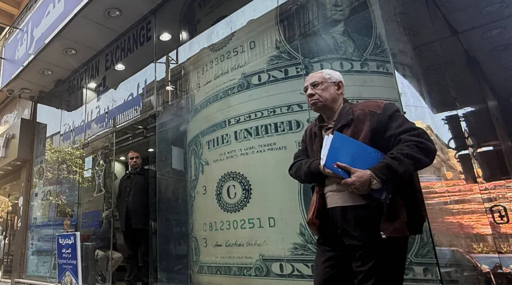 رجل مصري يمر أمام شاشة عرض لعملة الدولار الأميركي (رويترز)