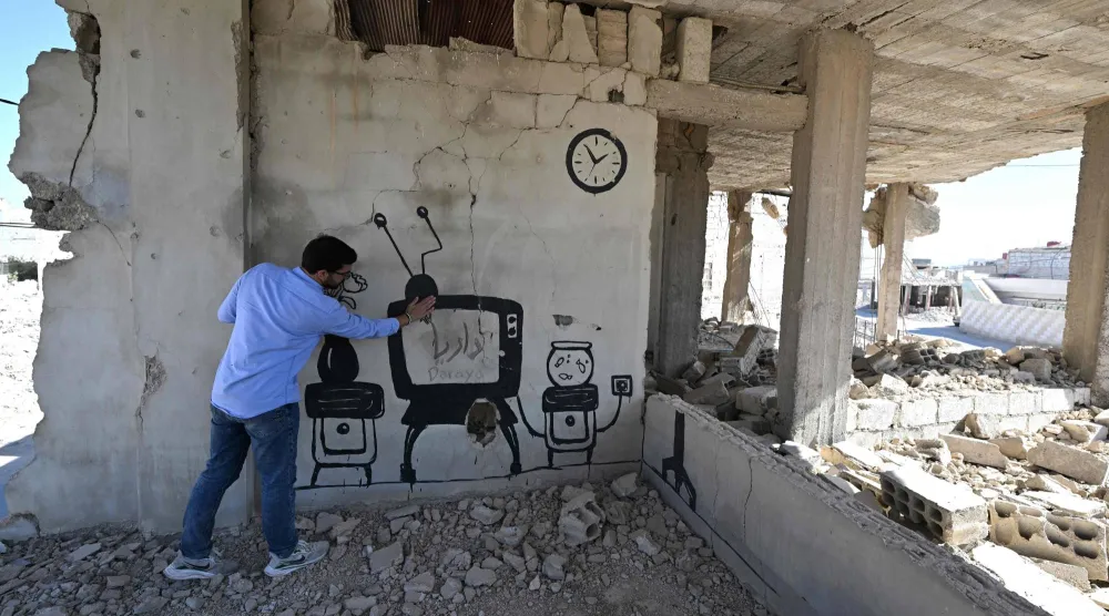 «بانكسي السوري» يشير إلى جدارية رسمها على جدار مبنى قبل فراره من داريا عام 2016 (أ.ف.ب)