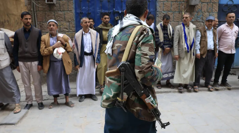 مسلح حوثي يمر أمام تجمع للسكان بحيّ في صنعاء (إ.ب.أ)
