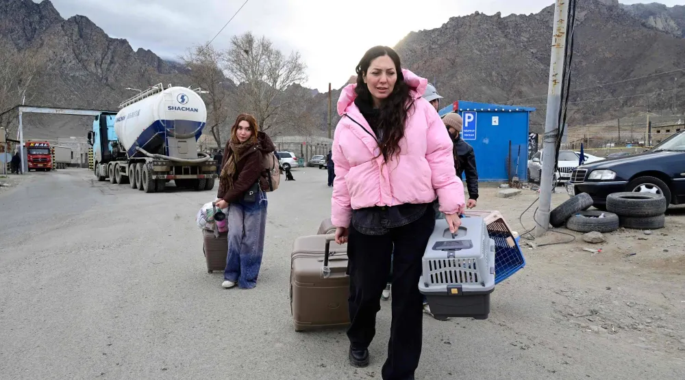 لاجئون يسيرون حاملين أمتعتهم بعد عبورهم الحدود من إيران إلى أرمينيا عند نقطة تفتيش حدودية في بلدة ميغري جنوب أرمينيا، 8 مارس 2026 (أ.ف.ب)